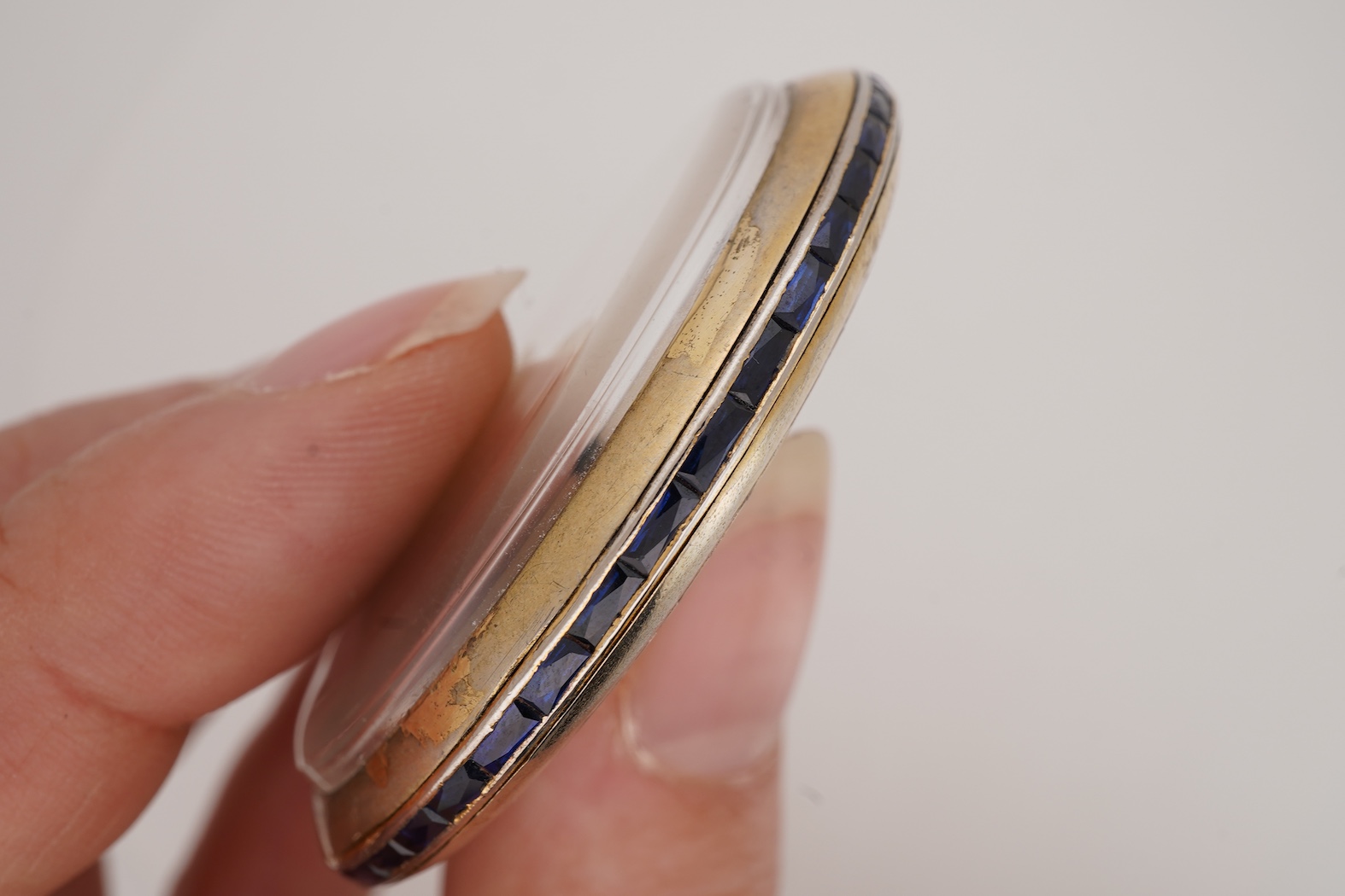 A French Art Deco parcel gilt white metal open faced dress pocket watch, with synthetic sapphire set border and winding crown